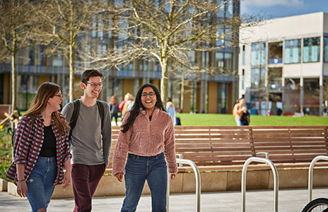 1 male and 2 female students talking as they work across the campus